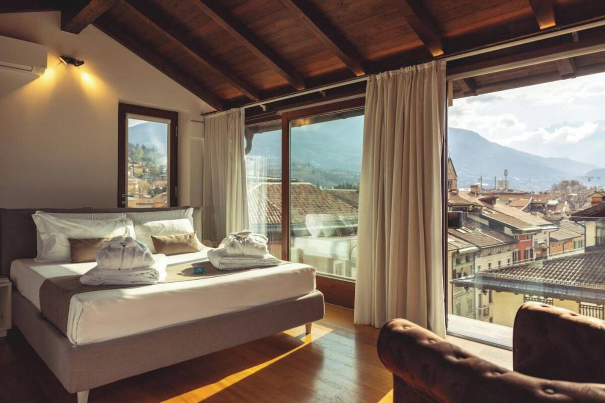A bedroom with a bed, a sofa, and large windows offering a city view.