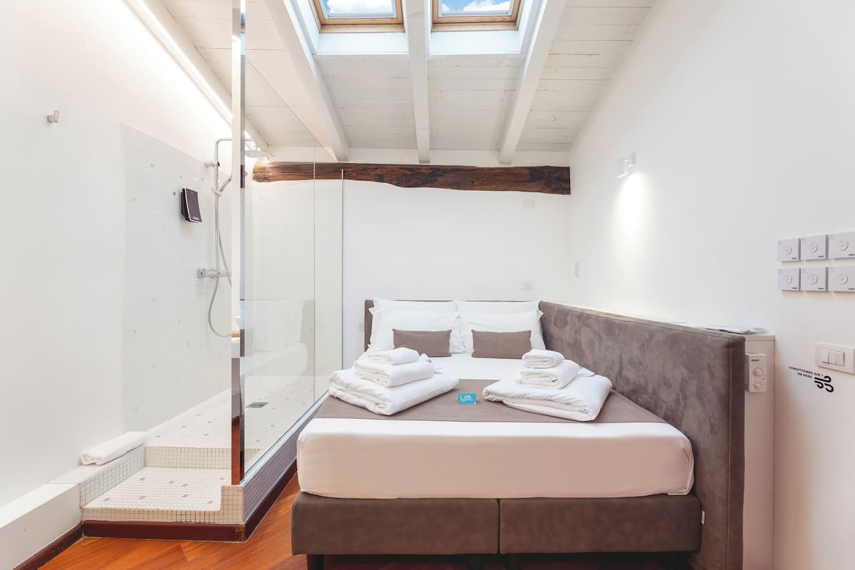A modern hotel room with a glass shower enclosure, a bed with neatly folded towels, and a skylight above.