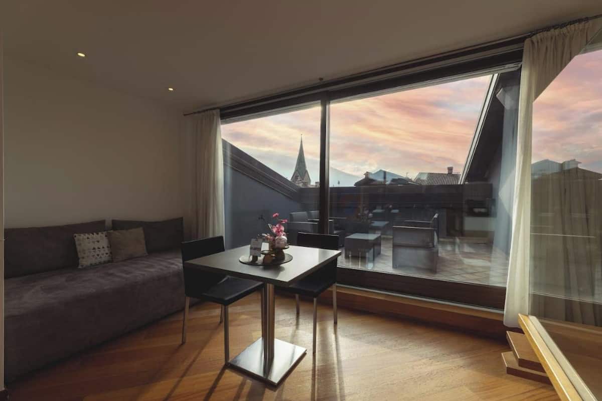 A modern living room with a large window, a sofa, a dining table, and a view of a cityscape.