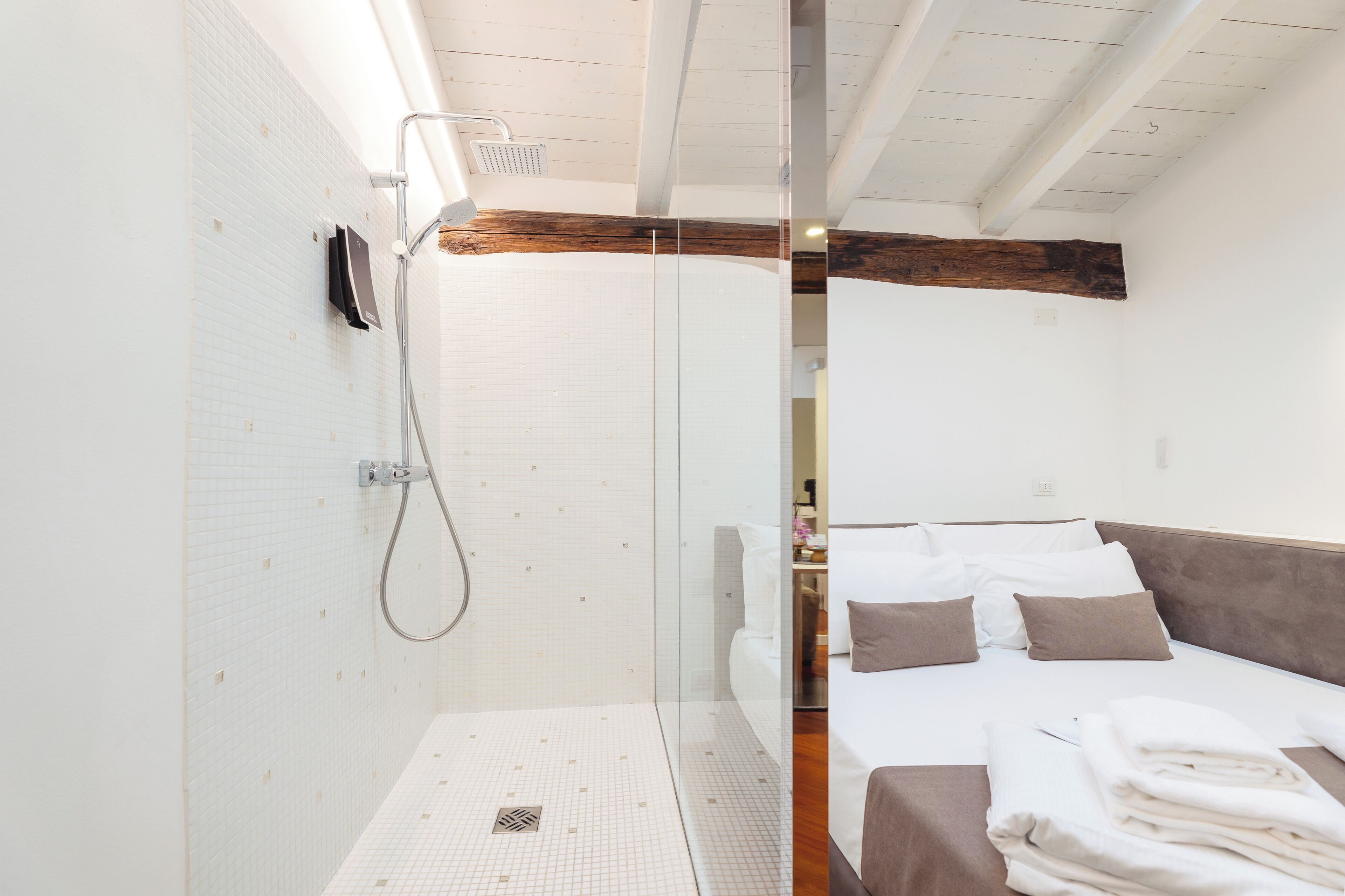 Un bagno moderno con box doccia in vetro, parete rivestita in piastrelle bianche e soffitto con travi in legno.