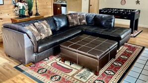 Una sala de estar con sofá modular, reposapiés, escalera de madera y mesa de futbolín.