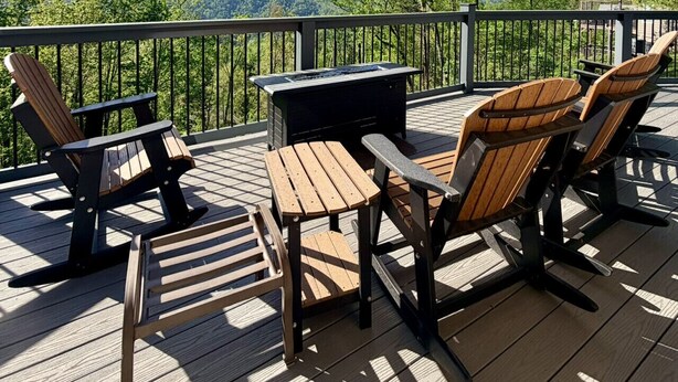 Una terraza con sillas Adirondack, una mesa y una parrilla, con vistas a un paisaje montañoso.