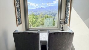 Una habitación con vistas a montañas, una mesa con dos sillas y elementos decorativos en las paredes.