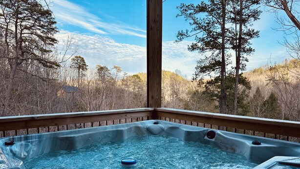 Un bain à remous avec une terrasse en bois et une vue sur les arbres et les collines.