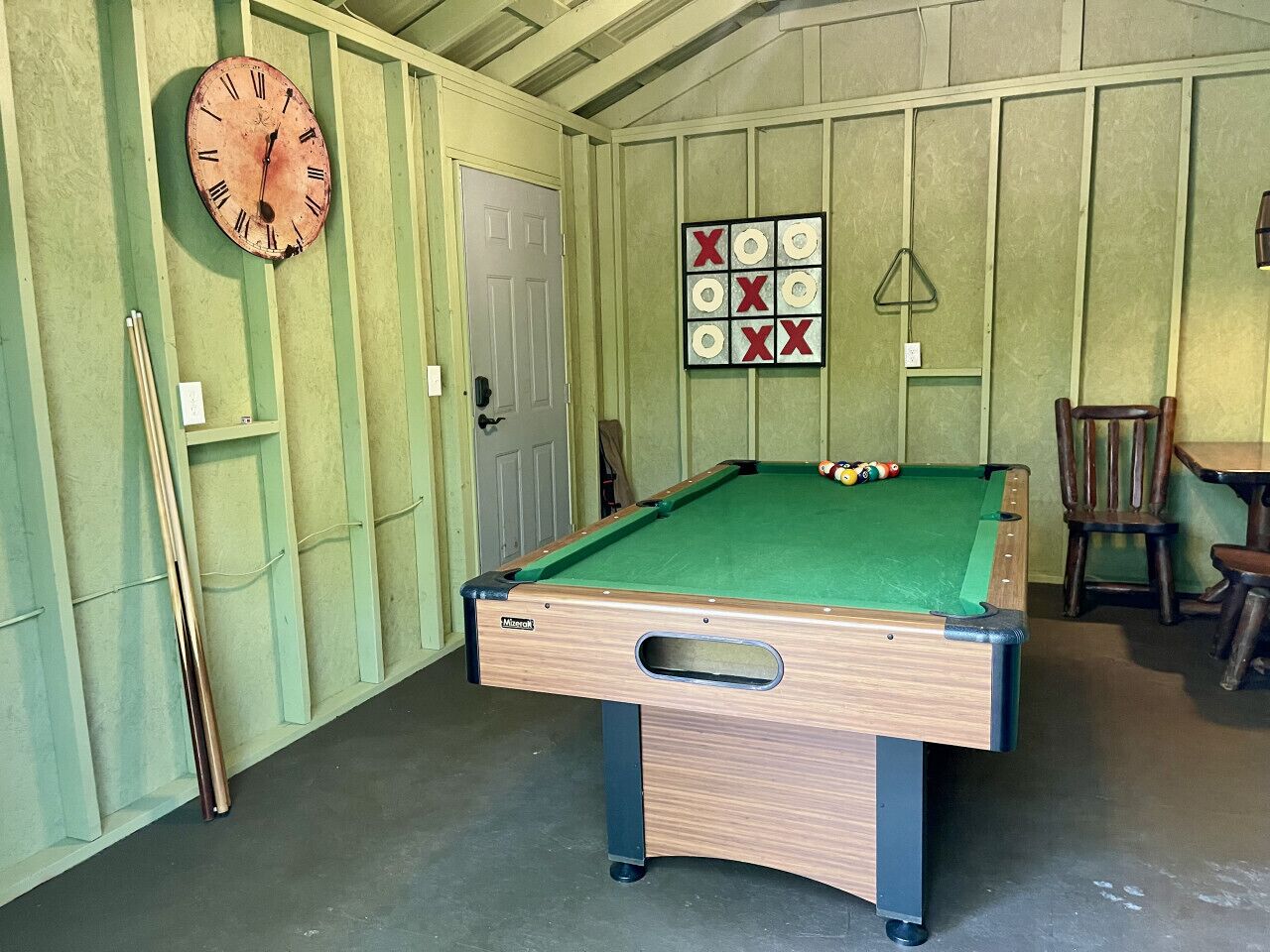 Uma mesa de bilhar em um quarto com paredes verdes e um relógio.