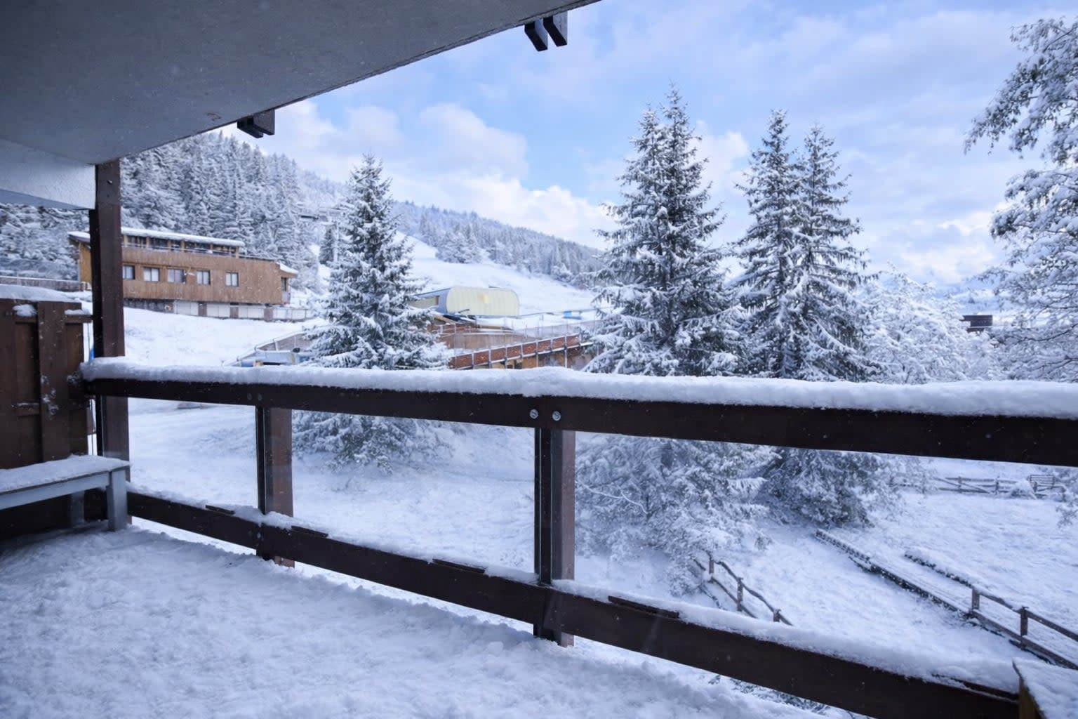 Un balcón cubierto de nieve con vistas a un paisaje nevado, que incluye árboles y un edificio al fondo.