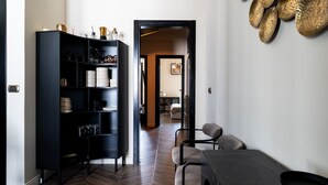 Una zona de menjador moderna amb taula i cadires de fusta fosca, un moble prestatges negre amb estris de cuina, i un passadís que condueix a una altra habitació.