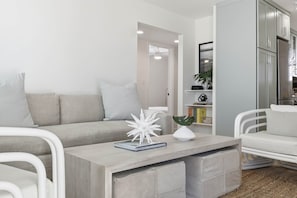 A modern living room with a grey sofa, white armchairs, a wooden coffee table, and a white decorative piece.