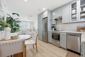 A modern kitchen with grey cabinets, stainless steel appliances, and a dining area with a white table and chairs.