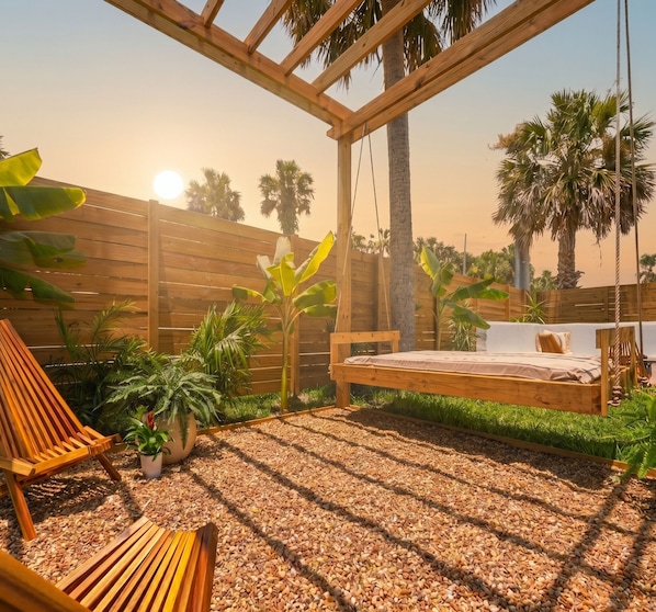 A wooden deck with a swing, a bench, and a bed with a view of palm trees.