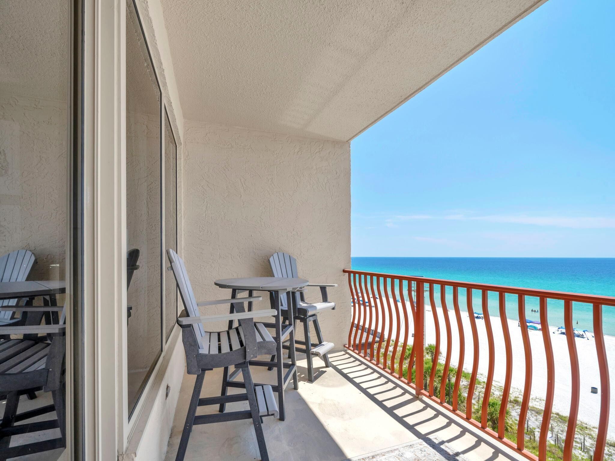 Un balcon avec deux chaises et une table, donnant sur une plage dont la rambarde est rouge.