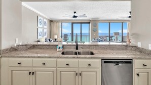 A kitchen with a stainless steel sink, white cabinets, and a dishwasher. There are ceiling lights and a ceiling fan.