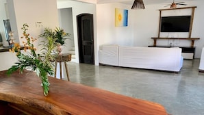 Un banco de madera con un florero en una sala de estar moderna, con un televisor y un cuadro en la pared.