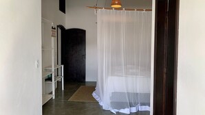 Un dormitorio con una cama bajo una mosquitera, una puerta de madera y una estantería.