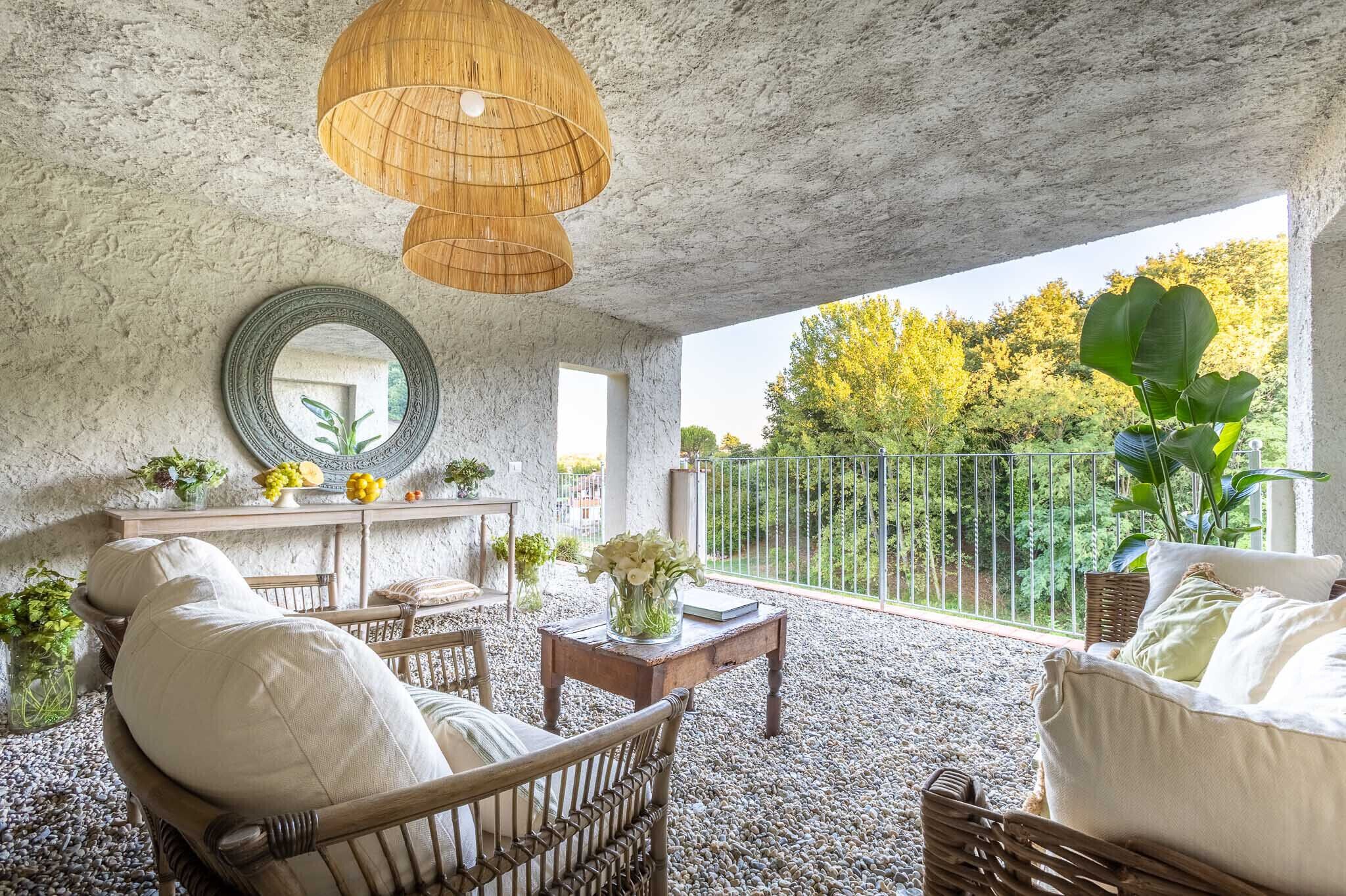 Une vaste terrasse dotée de meubles en osier, d’un miroir rond et d’un luminaire suspendu.