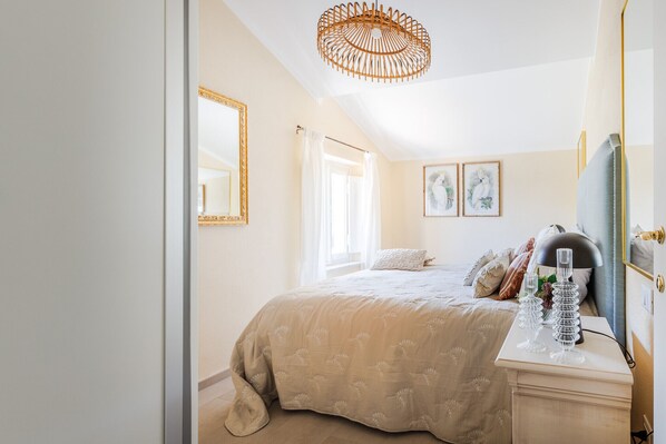 A bedroom with a large bed, a bedside table with decorative glassware, a mirror, and framed artwork on the wall.