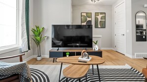 A modern living room with a flat-screen TV, wooden coffee table, and a potted plant. - Cowboy Chalet SE, AC, Games, King Bed, 20 min to Down Town (Calgary)