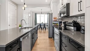 A modern kitchen with stainless steel appliances, a central island, and a dining area with a view. - Cowboy Chalet SE, AC, Games, King Bed, 20 min to Down Town (Calgary)