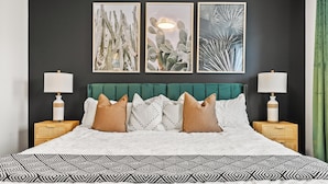 A bed with a white and black patterned bedspread, a green upholstered headboard, and multiple pillows. There are three framed artworks on the wall above the bed. - Cowboy Chalet SE, AC, Games, King Bed, 20 min to Down Town (Calgary)