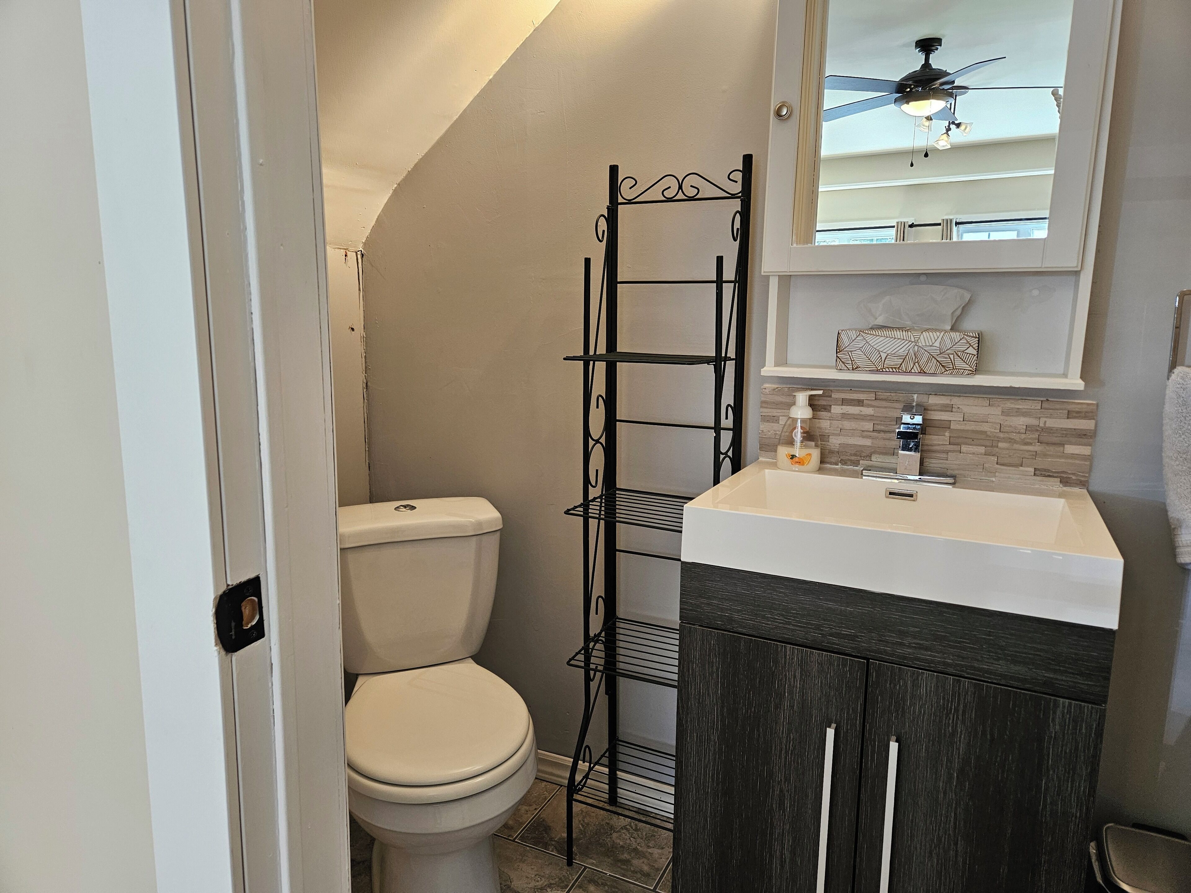Une petite salle de bain comprenant des toilettes, un meuble-lavabo avec un miroir et un ventilateur de plafond.
