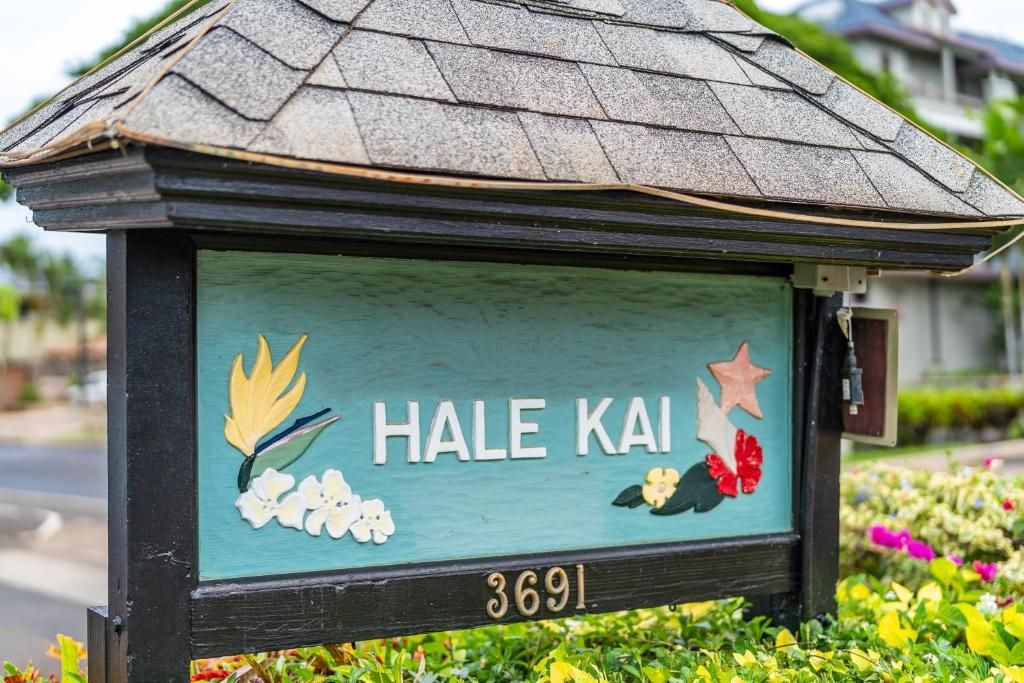 Een huisschild met de naam 'HALE KAI' en het nummer '3691' op een turquoise achtergrond met bloemversiering.