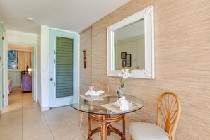 A dining area with a glass table, wicker chairs, and a mirror on the wall.
