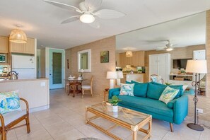 A spacious living area with a teal sofa, a glass coffee table, and a dining table with chairs.