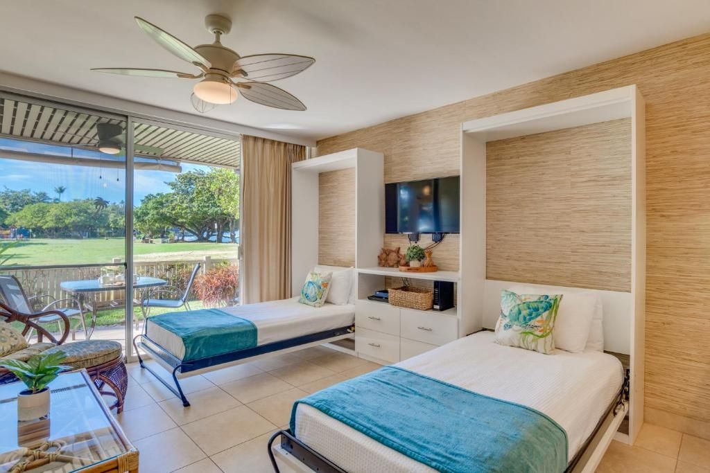 A hotel room with two beds, a TV, and a balcony with outdoor furniture.