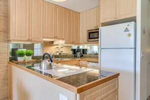 A kitchen with wooden cabinets, a stainless steel kettle, a microwave, and a refrigerator.