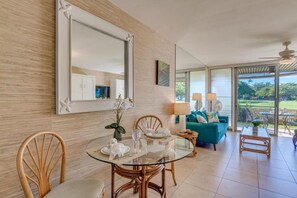 A dining area with a glass table, wicker chairs, and a sofa with a view through large windows.