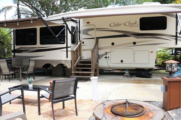 A recreational vehicle with a covered outdoor area, including a fire pit and outdoor furniture.