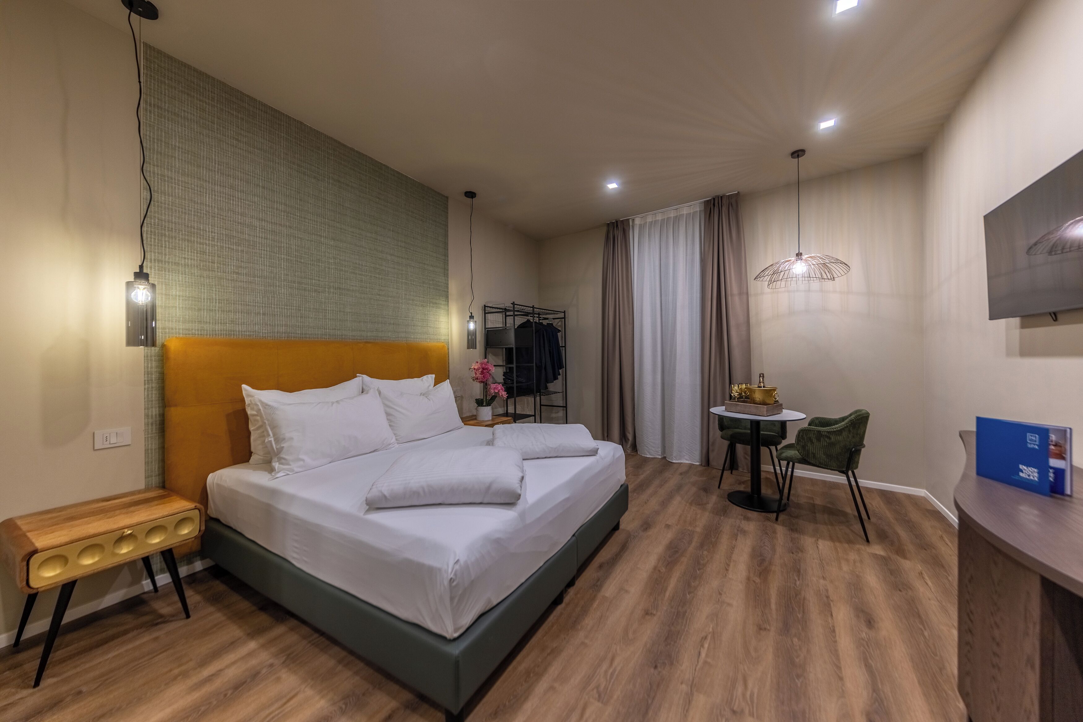 Ein modernes Hotelzimmer mit einem großen Bett, einem kleinen Schreibtisch, einem Sessel, einem Fernseher und einem Fenster mit Vorhängen.