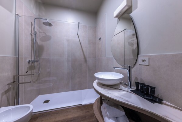 Un baño moderno con ducha de vidrio, lavamanos blanco y tocador con artículos de aseo.