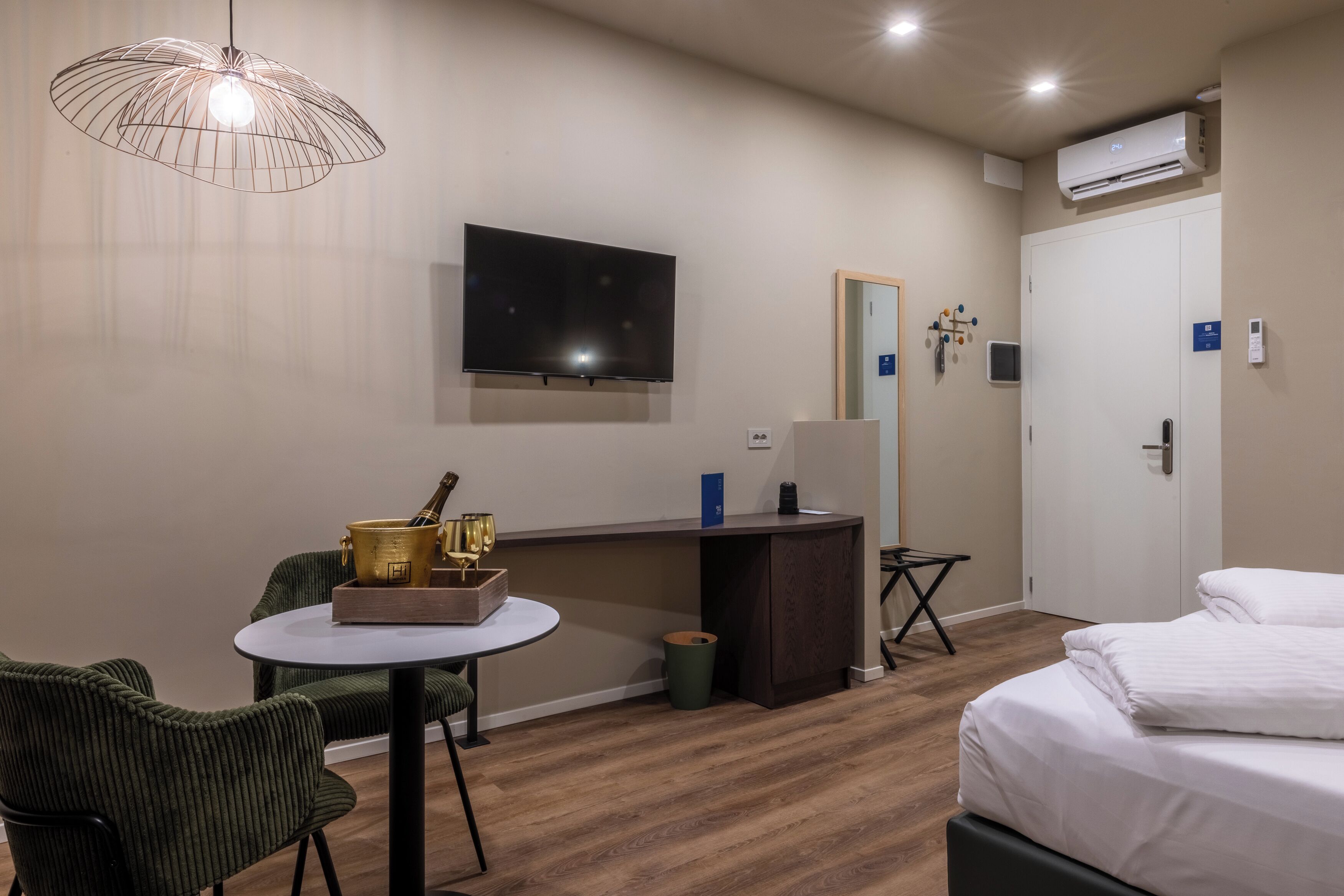 Habitación de hotel con cama, escritorio con silla, televisor y una mesita con lámpara.