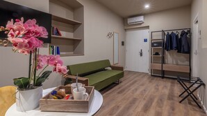 A modern room with a green sofa, a small table with a tray of snacks, a potted orchid, and a coat rack with jackets. - Soul of Trento San Martino (Trento)