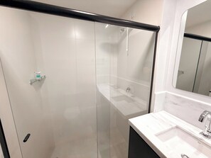 Ein modernes Badezimmer mit Duschkabine aus Glas, einem weißen Waschbecken mit Marmorplatte und einem großen Spiegel.
