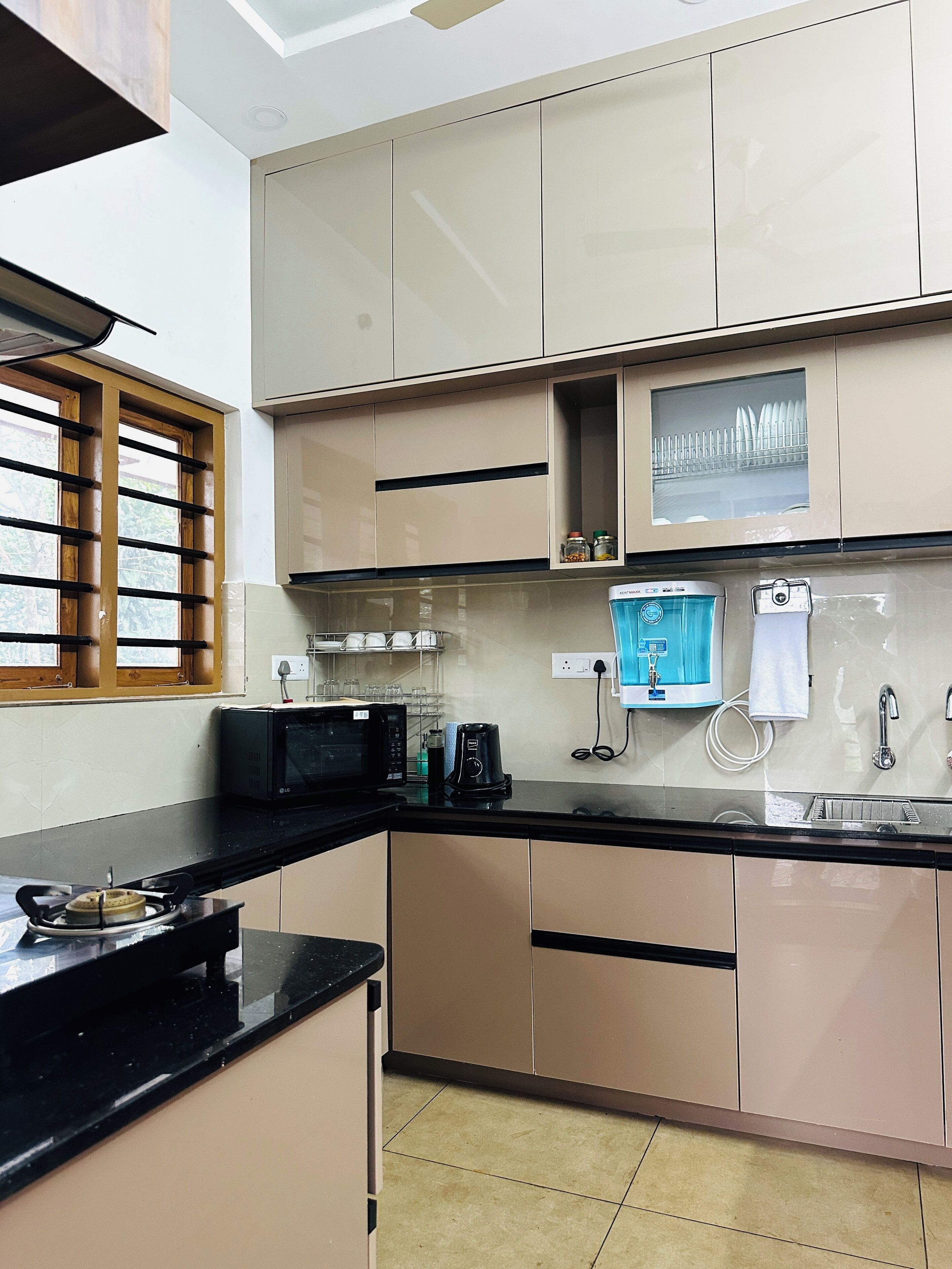 A modern kitchen with beige cabinets, a black countertop, a microwave, a coffee maker, and a window with wooden blinds.