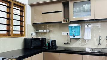 Eine moderne Küche mit beigen Schränken, einer schwarzen Arbeitsplatte, einer Mikrowelle, einer Kaffeemaschine und einem Fenster mit Holzjalousien.