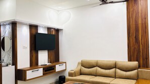 A modern living room with a beige sofa, a wooden coffee table, and a TV mounted on a wooden wall.