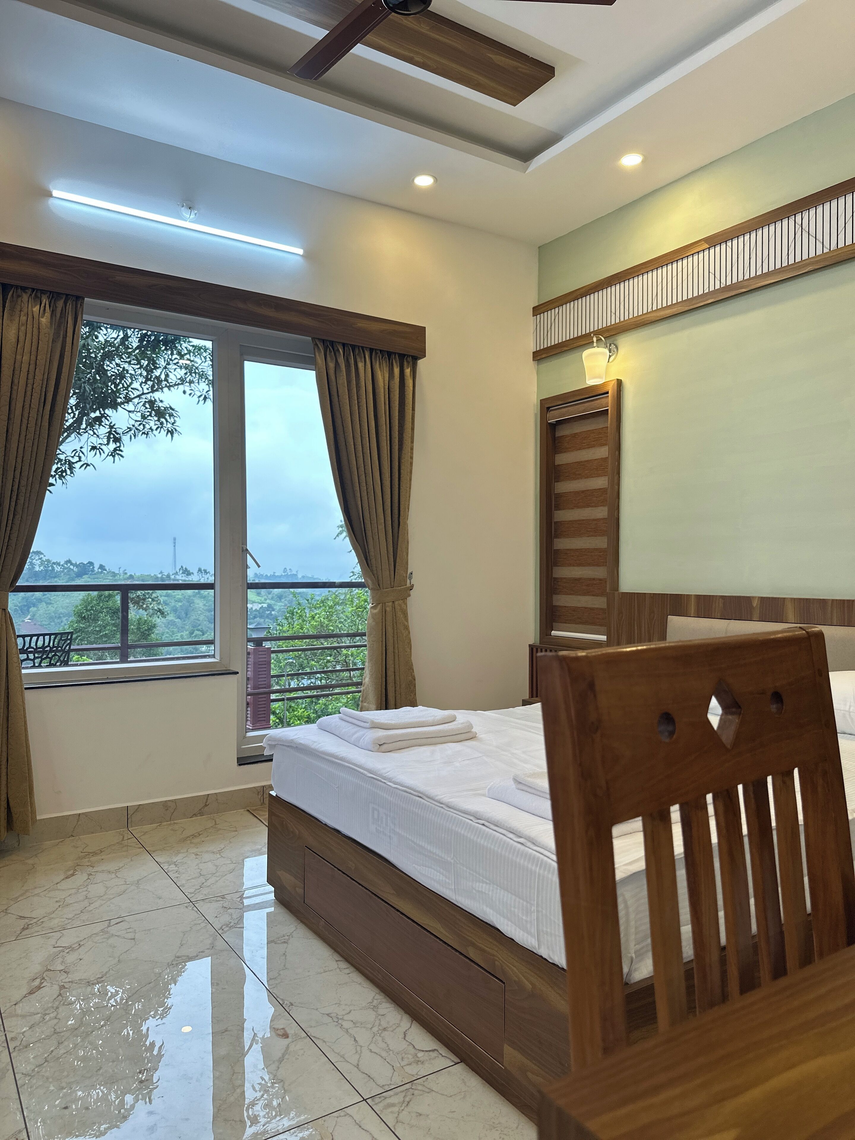 Una habitación de hotel con cama, cabecera de madera, ventana con cortinas, balcón e iluminación empotrada en el techo.
