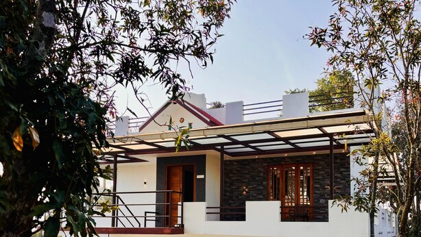 A two-story modern house with a stone facade, wooden doors, and a covered outdoor area.