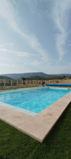 Une piscine rectangulaire à l’eau d’un bleu limpide, entourée d’une terrasse en béton et d’une zone herbeuse.