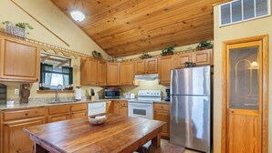 A kitchen with wooden cabinets, a stainless steel refrigerator, a wooden dining table, and a built-in oven. - River Cabin, Hot Tub, Sleeps 6! (Carroll County)