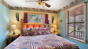 A bedroom with a large bed, a ceiling fan, two bedside lamps, a window with blinds, and a mural on the wall. - River Cabin, Hot Tub, Sleeps 6! (Carroll County)