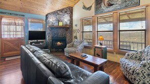 A cabin interior with a stone fireplace, leather sofa, and a television. - River Cabin, Hot Tub, Sleeps 6! (Carroll County)