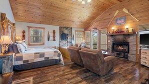 A cozy cabin interior with a wooden ceiling, a fireplace, a bed with a quilt, a sofa, and a sign reading "Lake Trout". - Cabin w/King Bed, Jacuzzi + View (Carroll County)