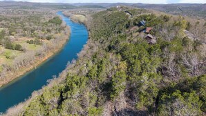 A river winding through a forested landscape with a few buildings on the right bank.