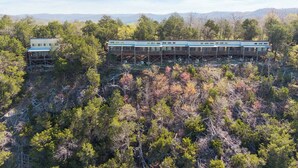 A cabin-style hotel with multiple rooms and a deck, surrounded by dense forest and mountains in the background.