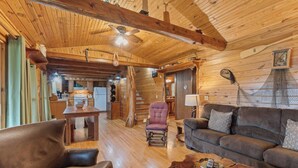Interior rústico de una cabaña con techo de madera, comedor, sofá y sillón de cuero.
