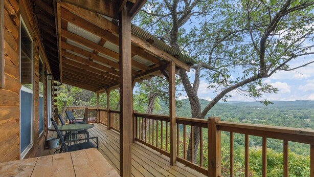 Una terraza de madera con una mesa y sillas, con vistas a un paisaje boscoso.